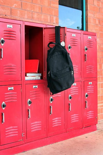 Books inside of a school locker with a black backpack hanging on the door.
